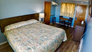 A room with a large bed, a desk with a chair, a small table, and a window with curtains. - Hillside Motel (Saint John)