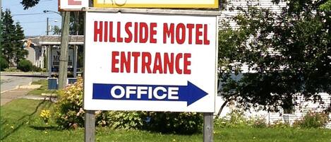 A motel sign with 'HILLSIDE MOTEL' and 'VACANCY' text, and an arrow pointing to the right for the entrance.