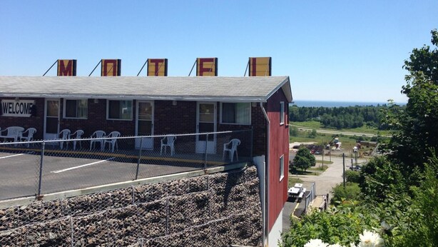 A building with a 'WELCOME' sign, a covered seating area with chairs, and a view of the landscape. - Hillside Motel (Saint John)
