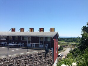 A building with a 'WELCOME' sign, a covered seating area with chairs, and a view of the landscape. - Hillside Motel (Saint John)