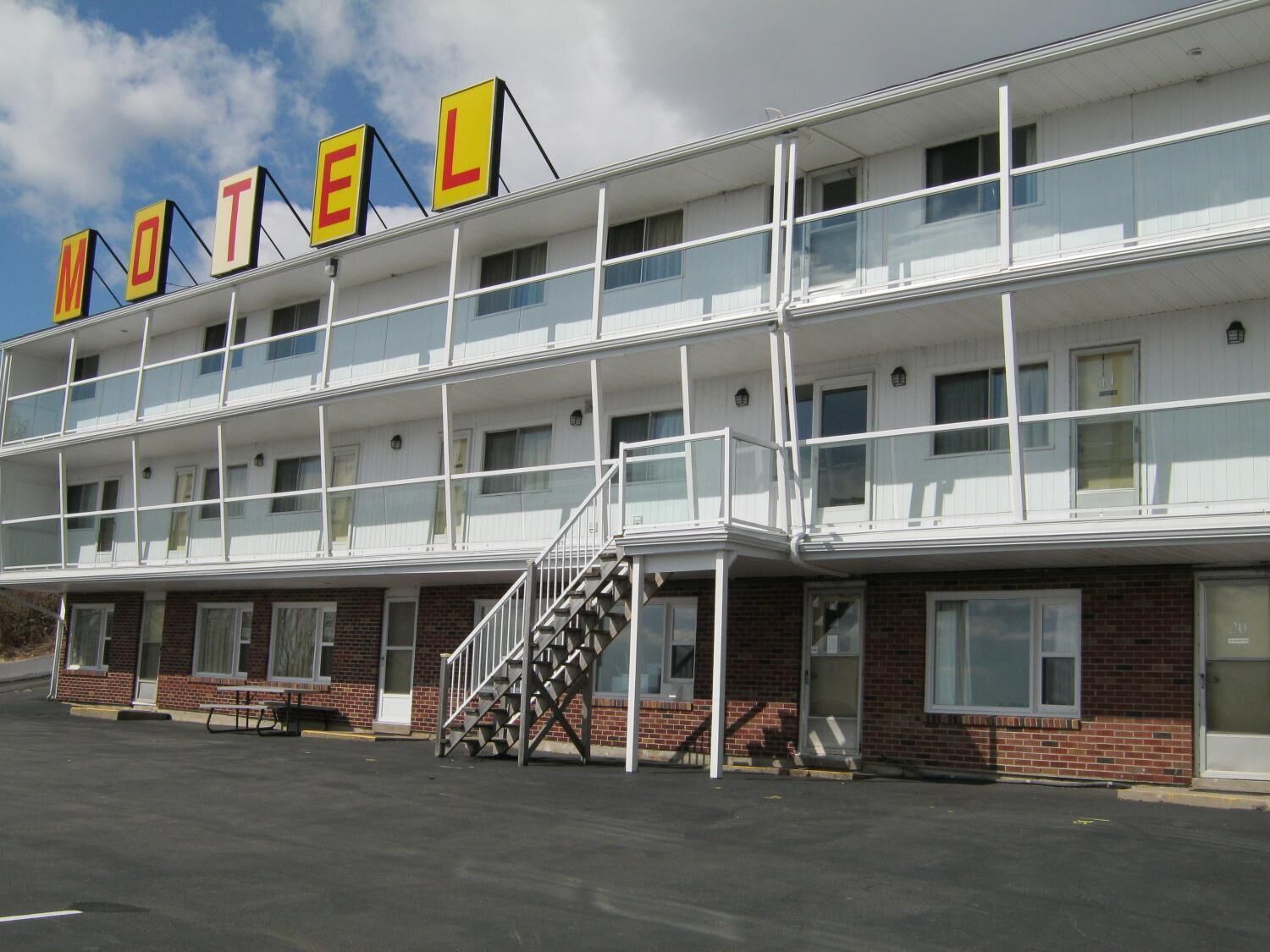 A motel with a two-story structure, a covered parking area, and a staircase leading to the entrance.