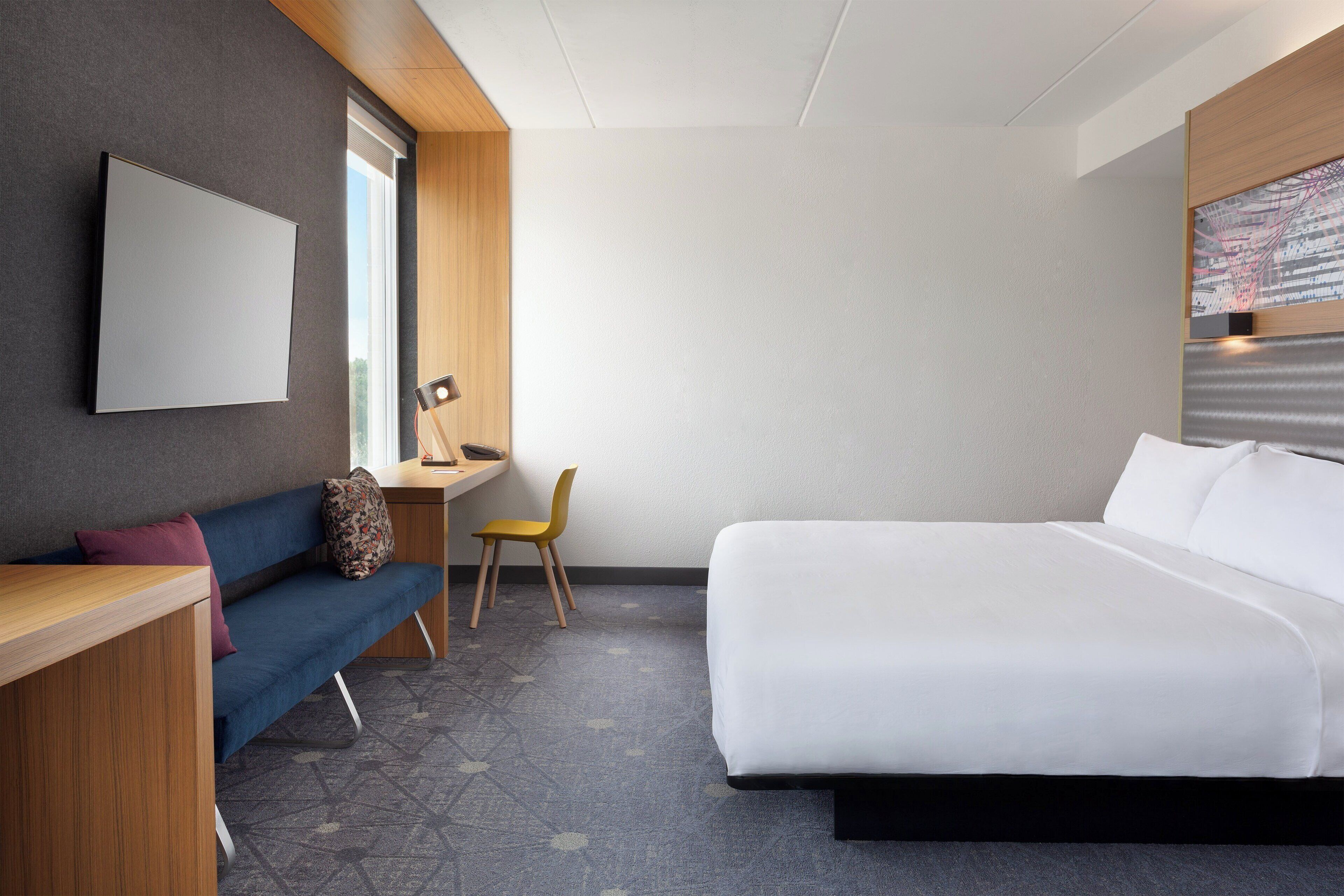 Una habitación de hotel moderna con cama, escritorio, silla y sofá.