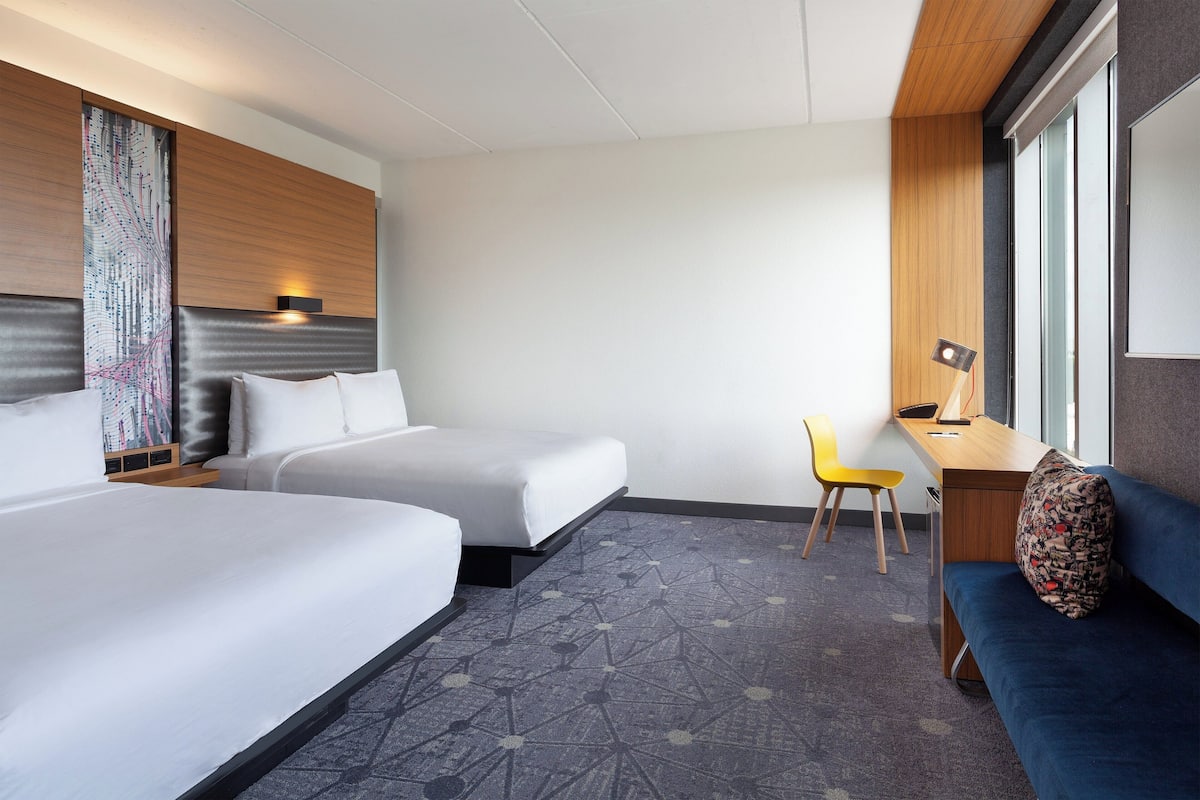 A hotel room with two beds, a desk, a chair, and a sofa.