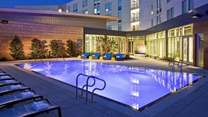 A modern hotel with a swimming pool, outdoor seating, and a well-lit building facade.