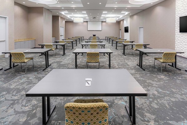 A conference room with multiple tables and chairs, a projector screen, and a television on the wall.