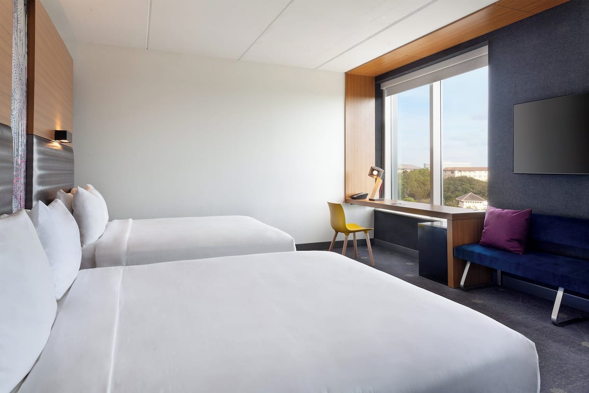 A hotel room with two beds, a desk, a chair, and a TV mounted on the wall.