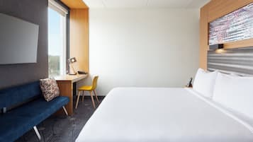 Una habitación de hotel con cama, escritorio, silla y un amplio ventanal.
