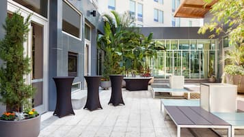 An outdoor patio area with modern seating, potted plants, and a glass enclosure.