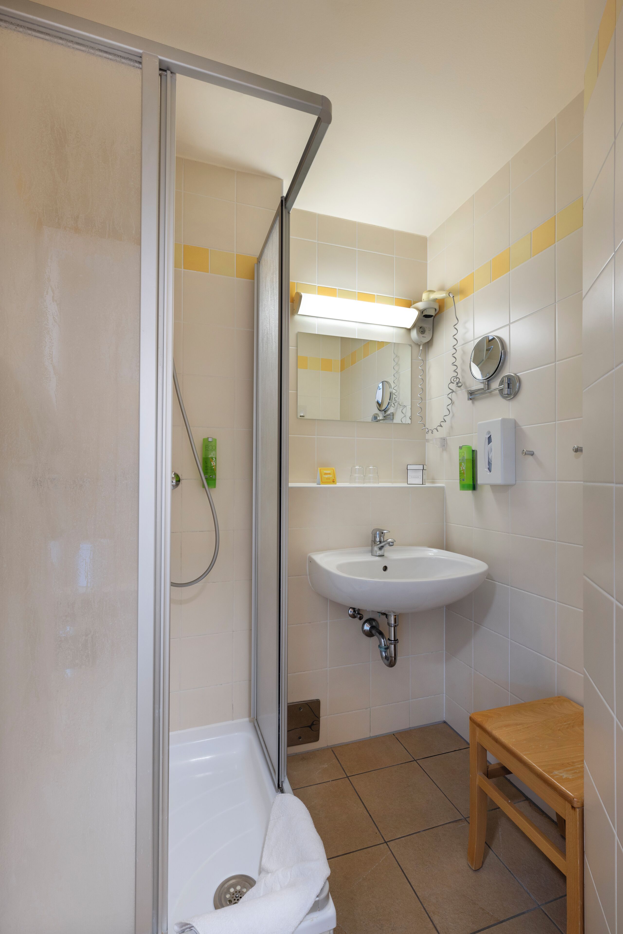 A bathroom with a shower, sink, and a wooden stool.