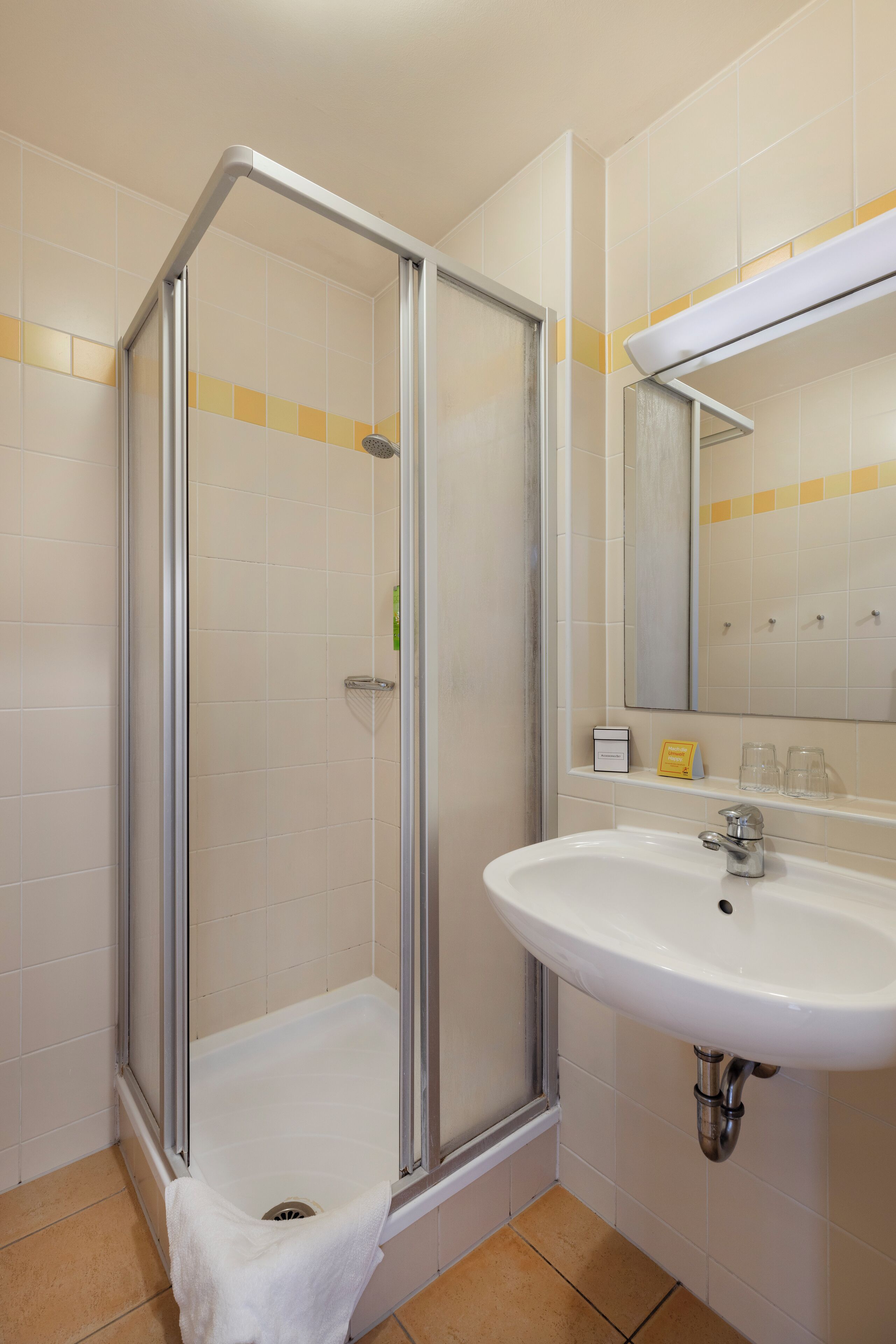 Una ducha con puerta de cristal, un lavamanos con espejo y una toalla colgada en la puerta.