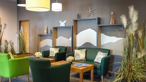 Un espace de détente moderne avec des canapés verts, des tables en bois et des œuvres d’art décoratives murales.