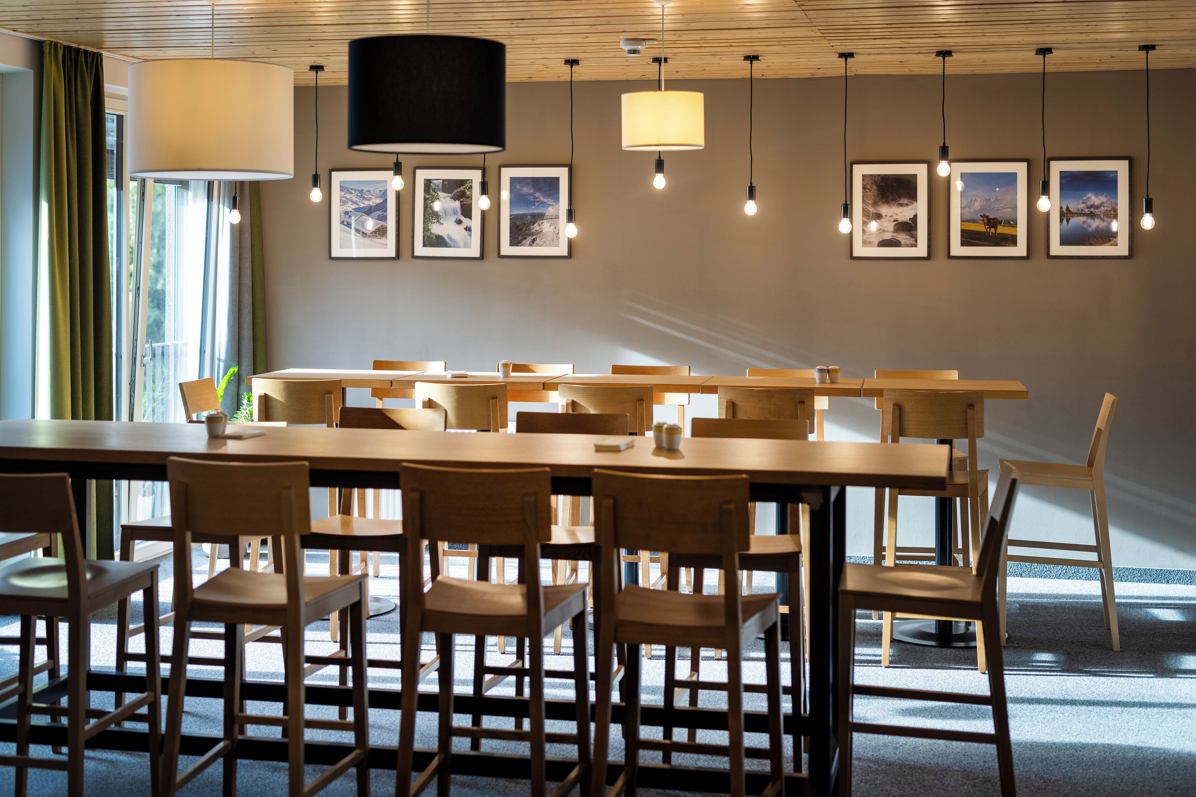 A dining area with wooden tables and chairs, framed pictures on the wall, and pendant lighting.