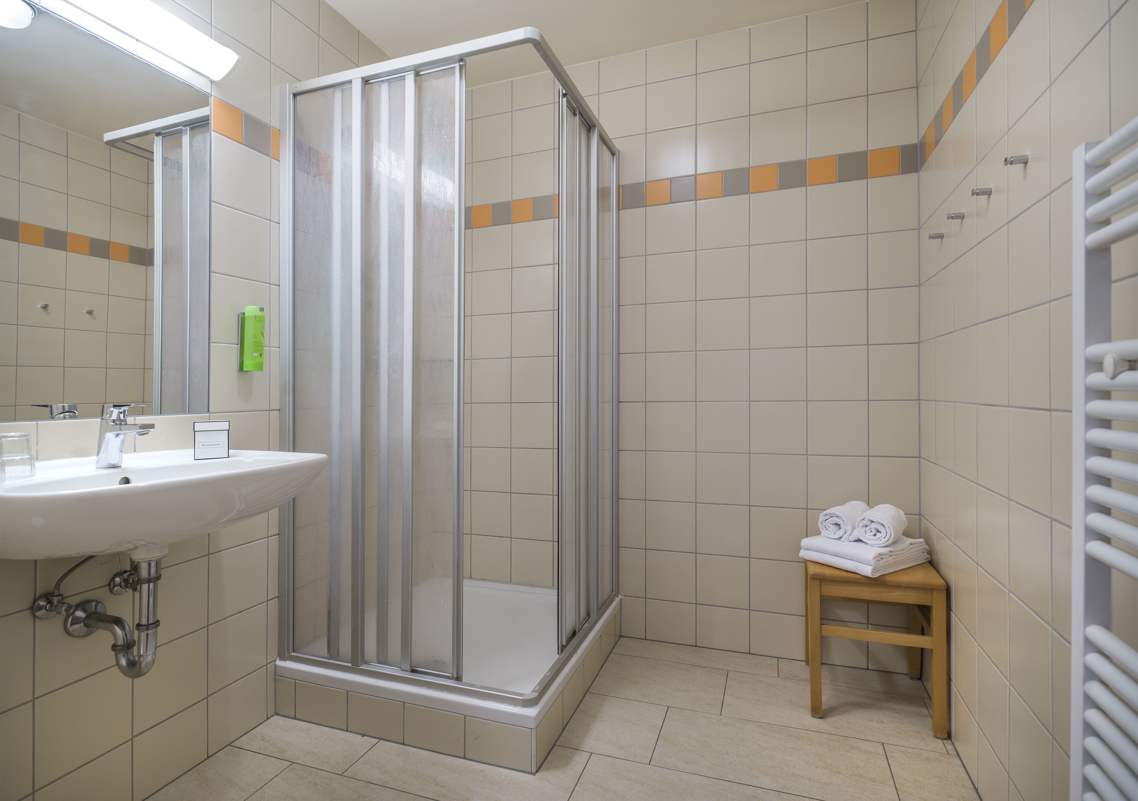 A bathroom with a shower enclosure, a sink, and a small table with towels.
