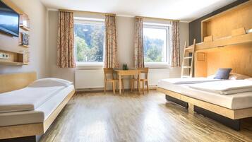 Een moderne hotelkamer met een houten vloer, een bureau met stoelen, een stapelbed en een televisie aan de muur.