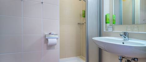 Une salle de bain avec une douche, du papier toilette et un lavabo avec un miroir.