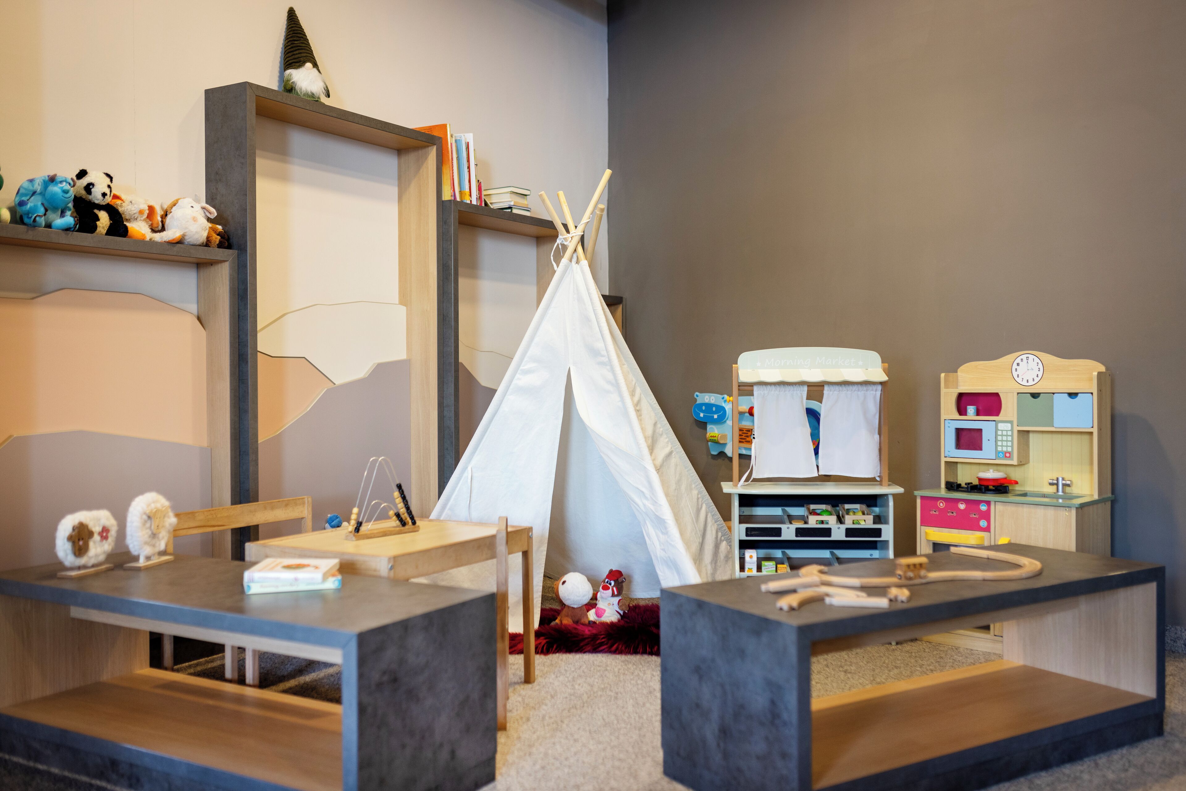 A children's playroom with a teepee, play kitchen, and storage shelves.