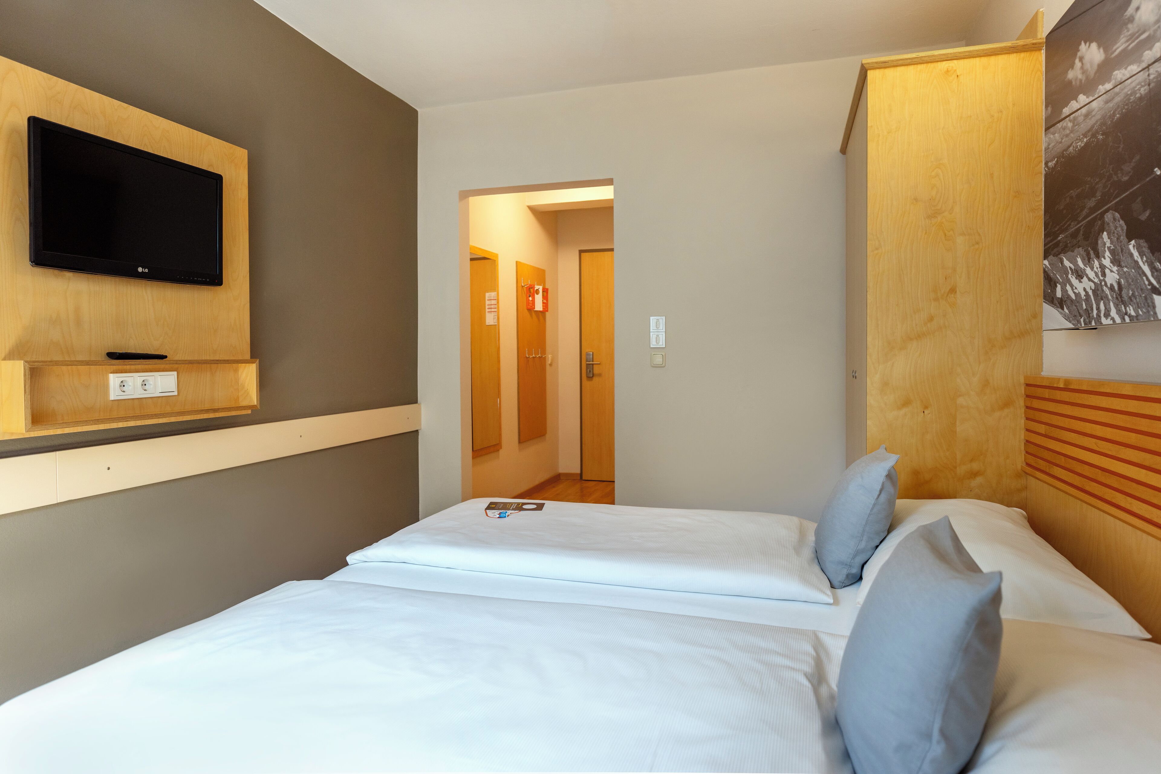 A hotel room with a bed, a mounted TV, and a wooden headboard.