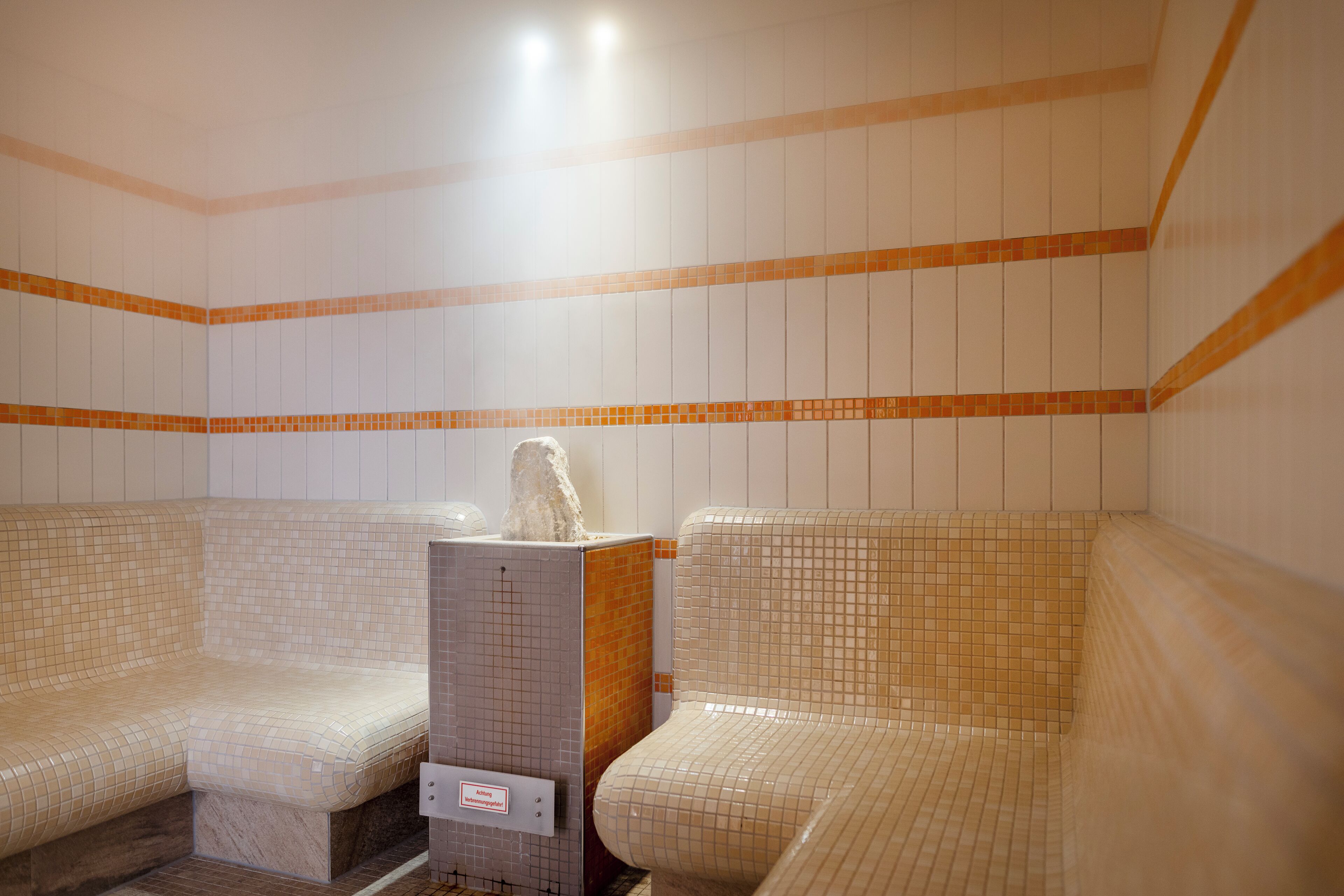 Un baño con baldosas, dos bancos y una columna central.