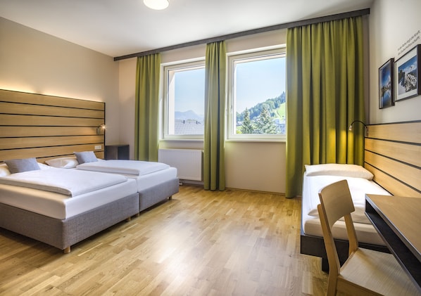 Habitación de hotel con dos camas, un escritorio y vistas a un paisaje montañoso.