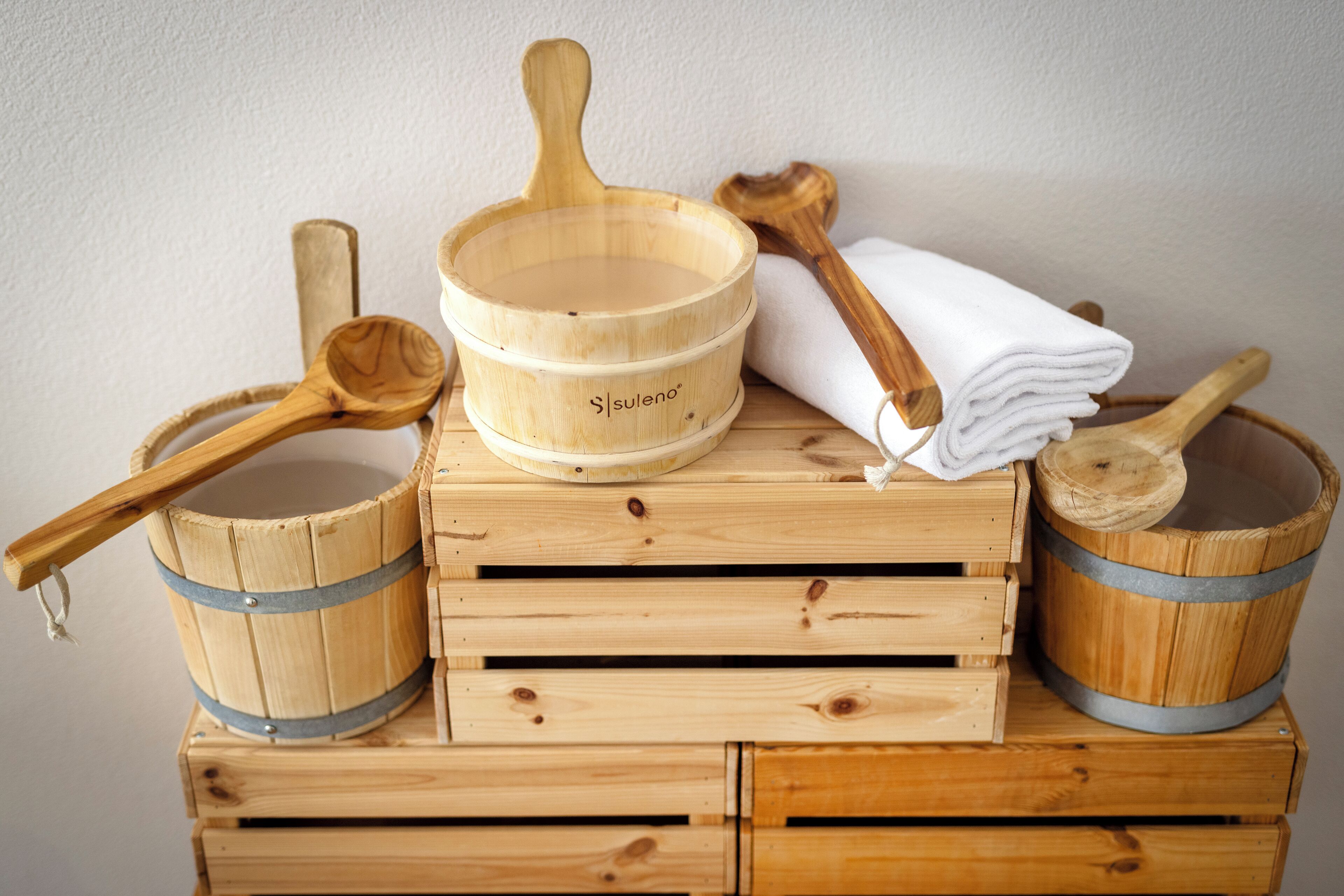 Houten emmers, een houten pollepel en een stapel witte handdoeken op houten kratten.