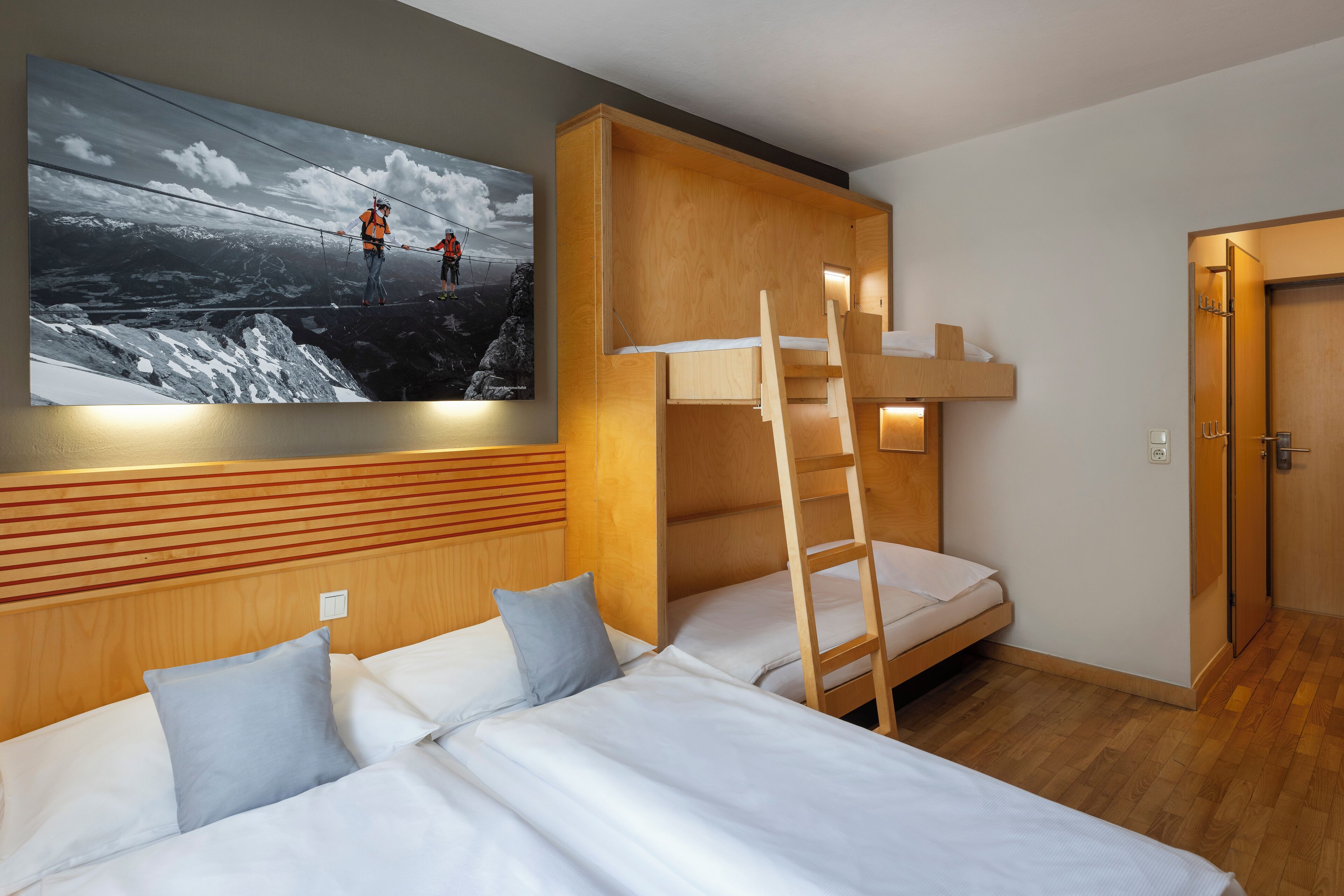 Habitación de hotel con literas, cabecera de madera, un cuadro de escaladores y una puerta de madera.