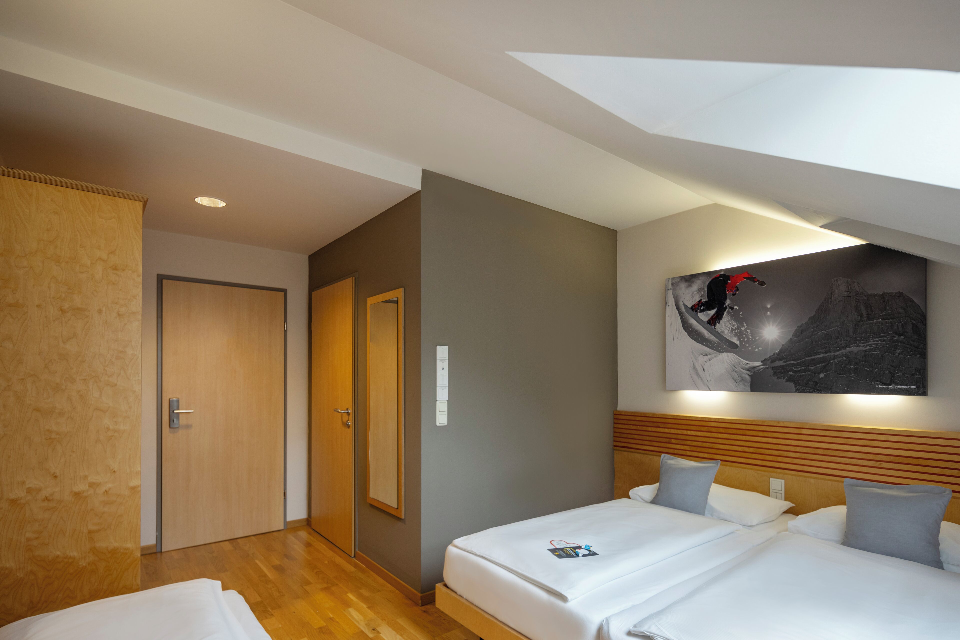 Habitación de hotel con dos camas, cabecero de madera, un cuadro en la pared y una puerta de madera.