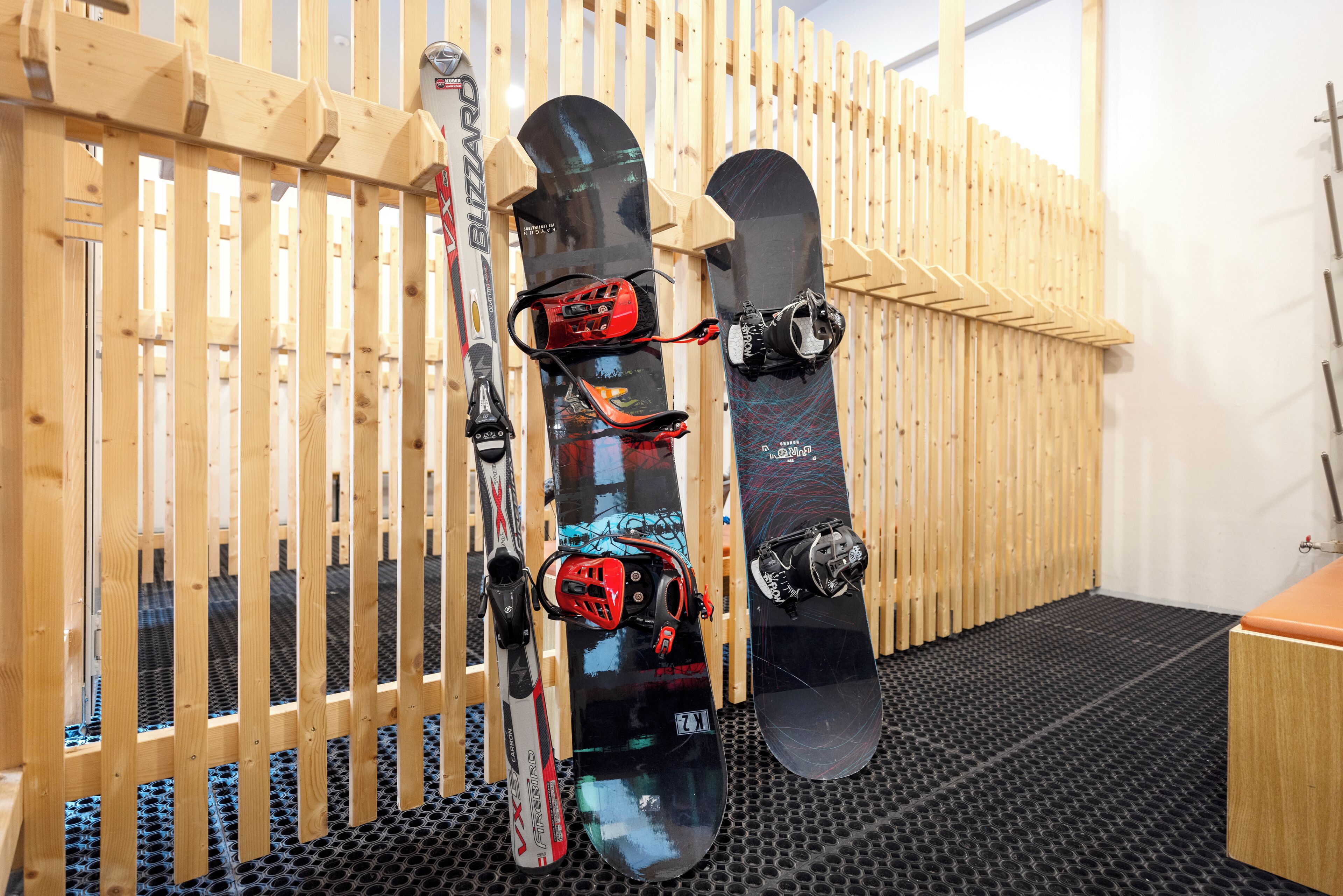 Tres tablas de snowboard apoyadas contra una pared de madera en una habitación con piso de goma negra.