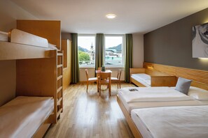 Une chambre d’hôtel avec des lits superposés, un canapé, une table avec des chaises et une vue sur un immeuble doté d’une tour.