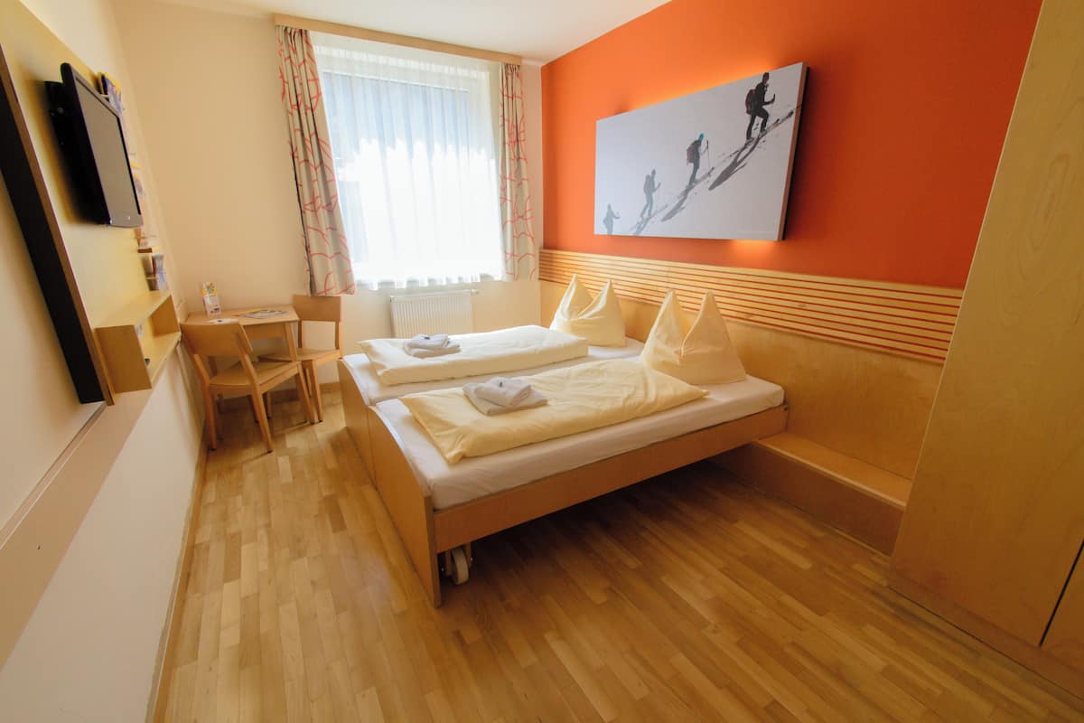 Habitació d'hotel amb sòl de fusta, dos llits individuals, escriptori amb cadira, radiador i un quadre gran a la paret.