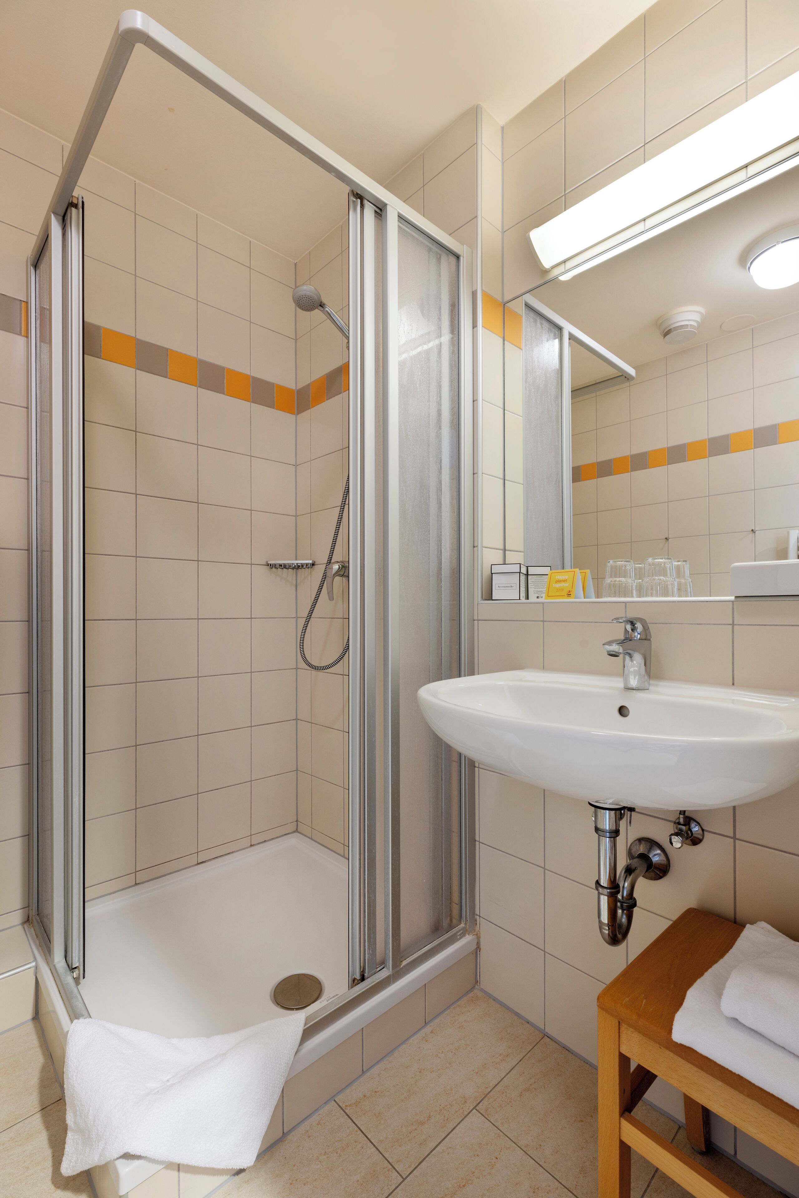 Un baño moderno con ducha de vidrio, un lavamanos blanco y un banco de madera.