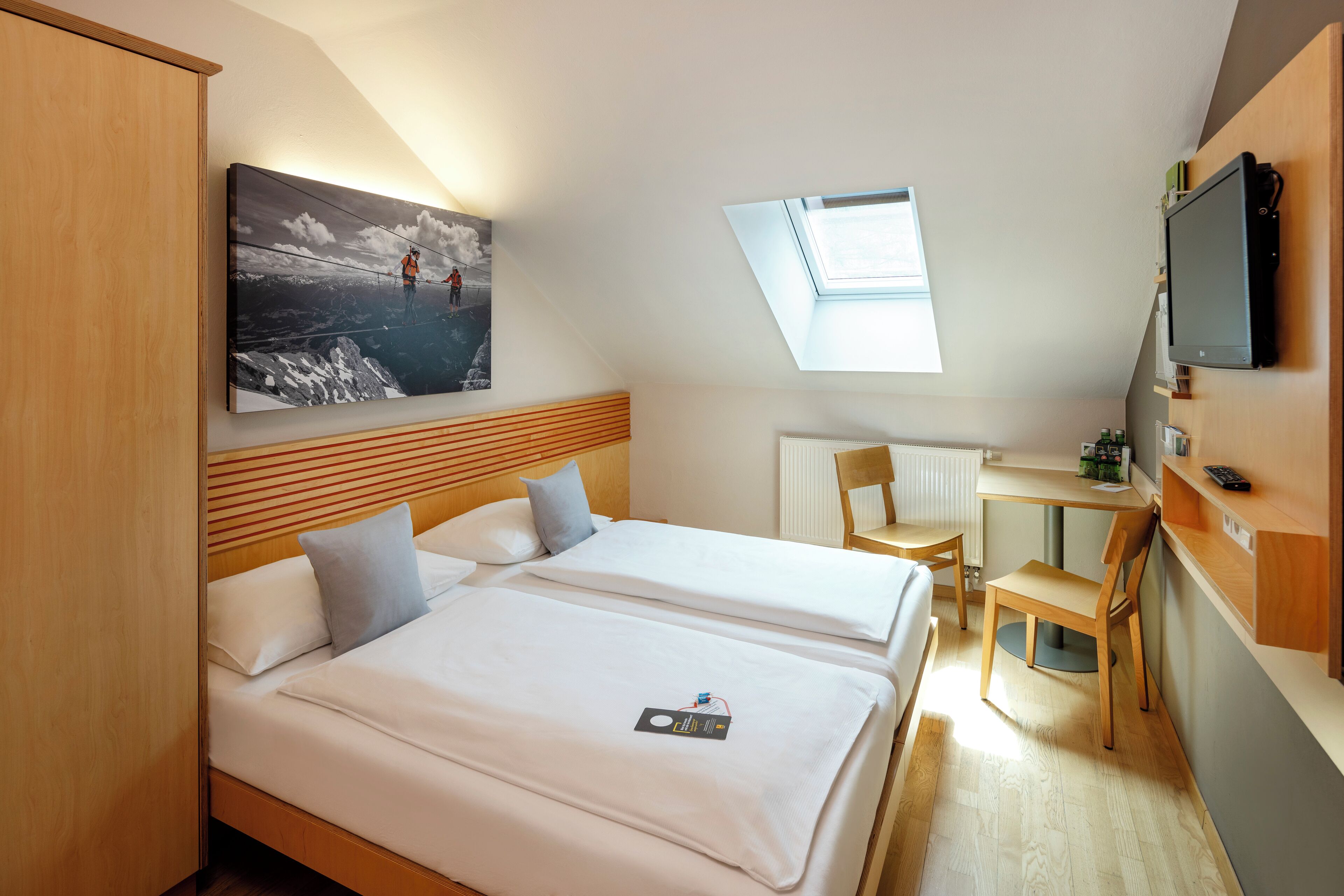 Een hotelkamer met twee bedden, een bureau, een stoel, een televisie en een dakvenster.