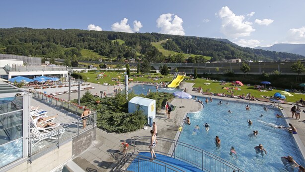 Un espace piscine comprenant plusieurs bassins, un toboggan aquatique et une vue sur une colline boisée.