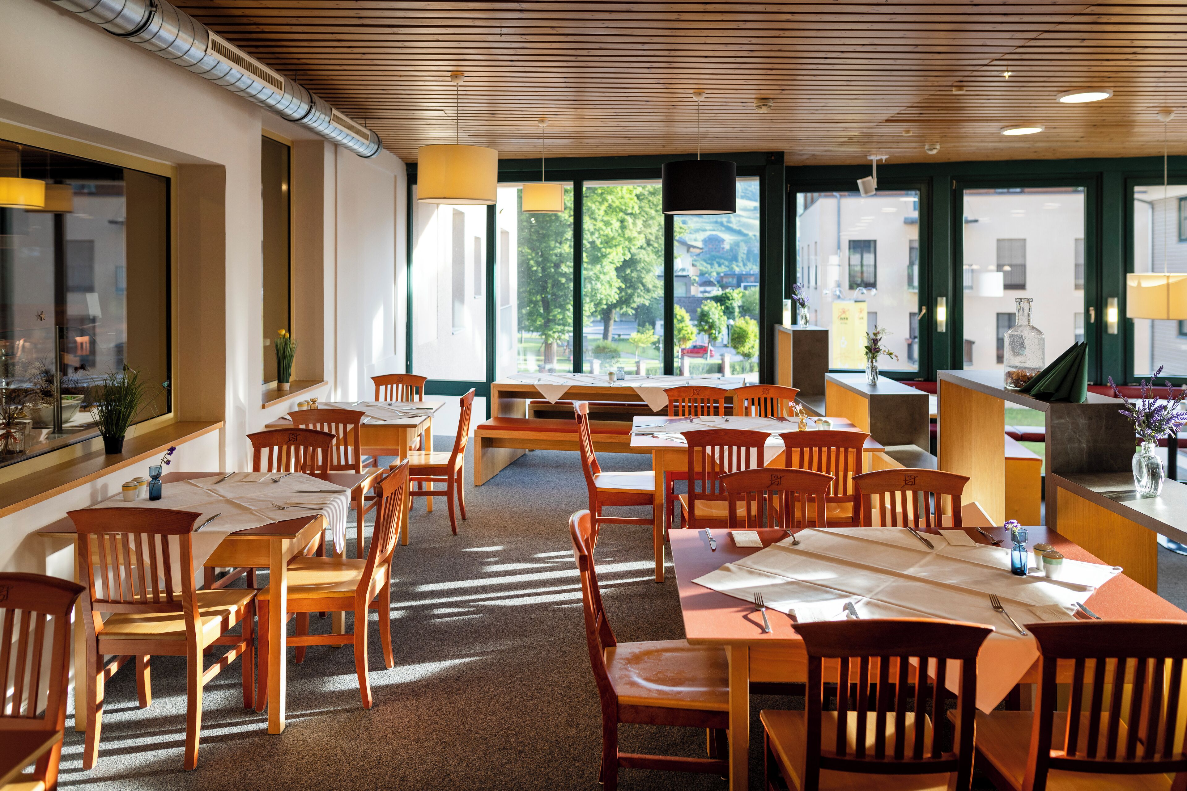 A restaurant with wooden tables and chairs, large windows, and a view of the outdoors.