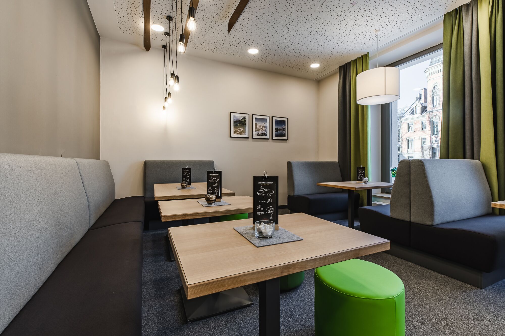 Een moderne hotelkamer met een zithoek, houten tafels en een groene poef.