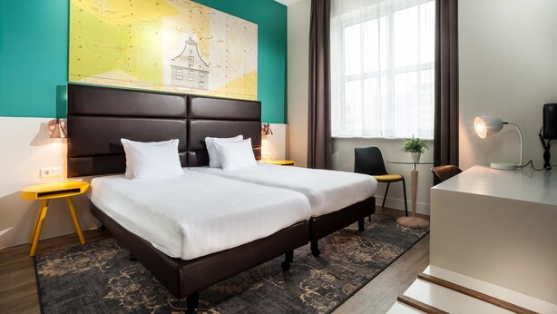 Une chambre d’hôtel avec un grand lit, un bureau, une chaise, une carte accrochée au mur et une fenêtre avec des rideaux.