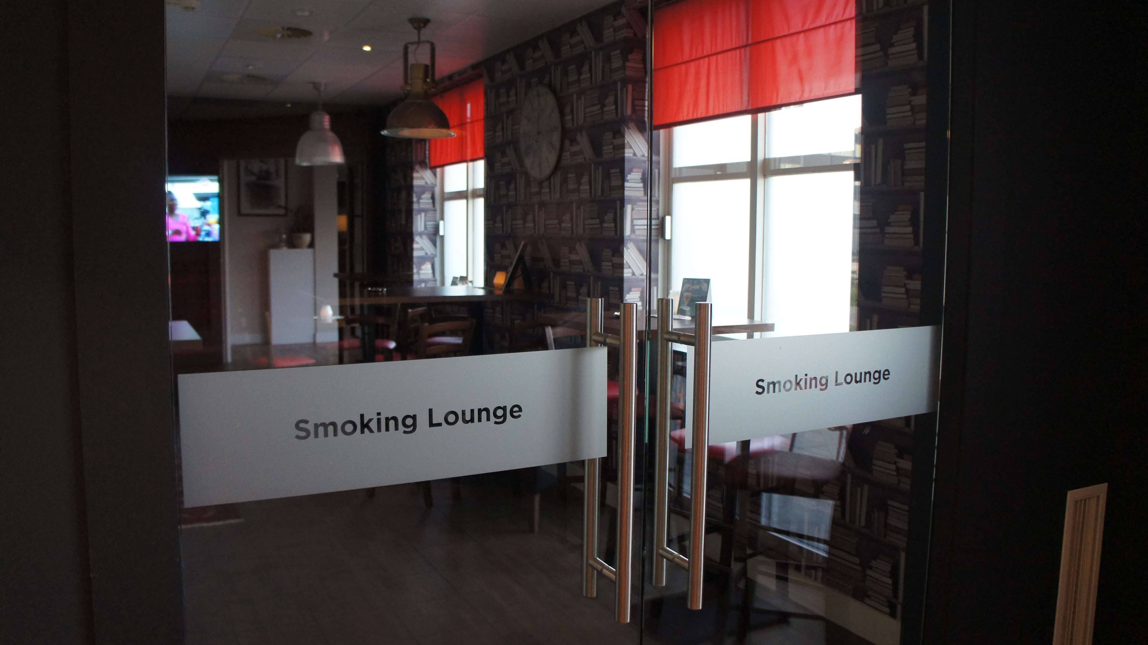Un salon pour fumeurs avec un panneau indicateur, des étagères en bois et une horloge au mur.