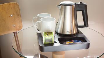 A glass table with a coffee maker, two white mugs, and a pack of pickwick tea.