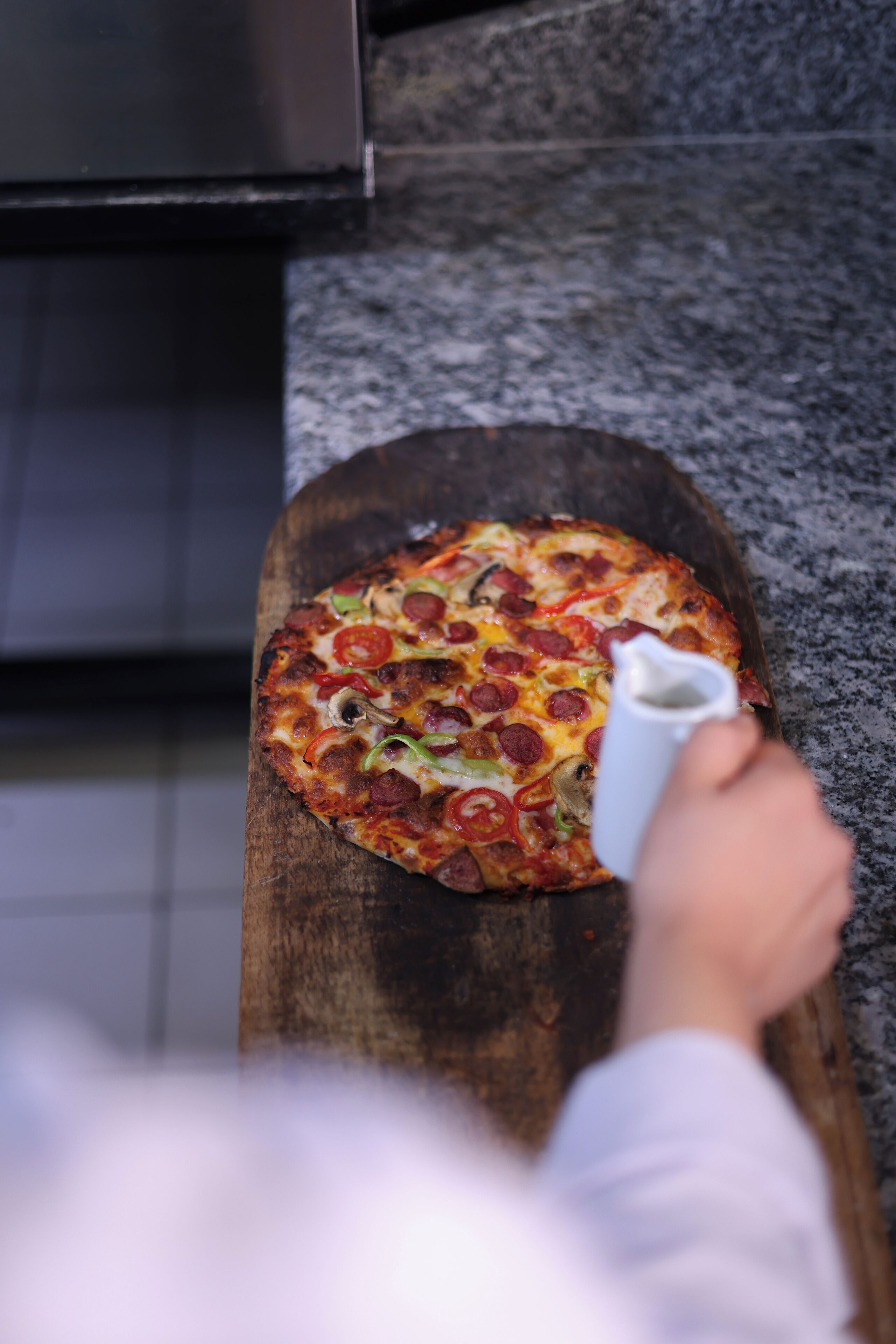 Uma pizza sobre uma tábua de madeira em uma cozinha.