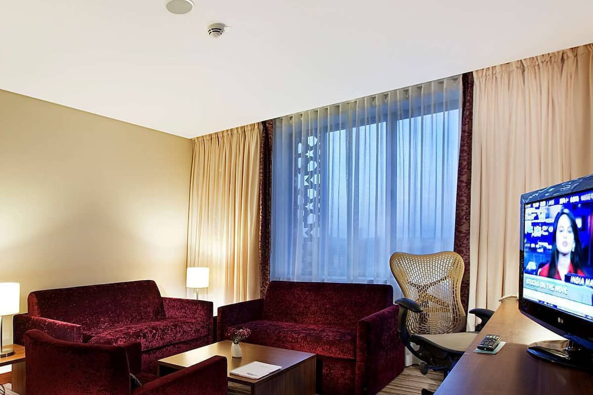 A hotel room with a large window, a television, and two red armchairs.