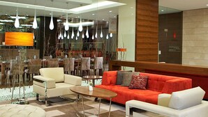 A modern lobby with a red sofa, white armchairs, and a round coffee table. There are hanging pendant lights and a large lamp. - Hilton Garden Inn Konya, Turkey (Konya)