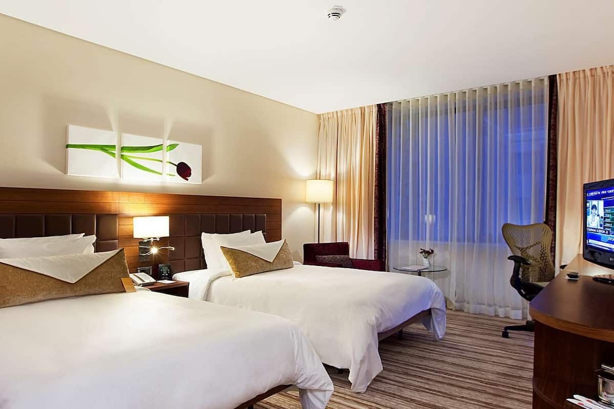 A hotel room with two beds, a desk, a chair, a television, and a window with curtains.