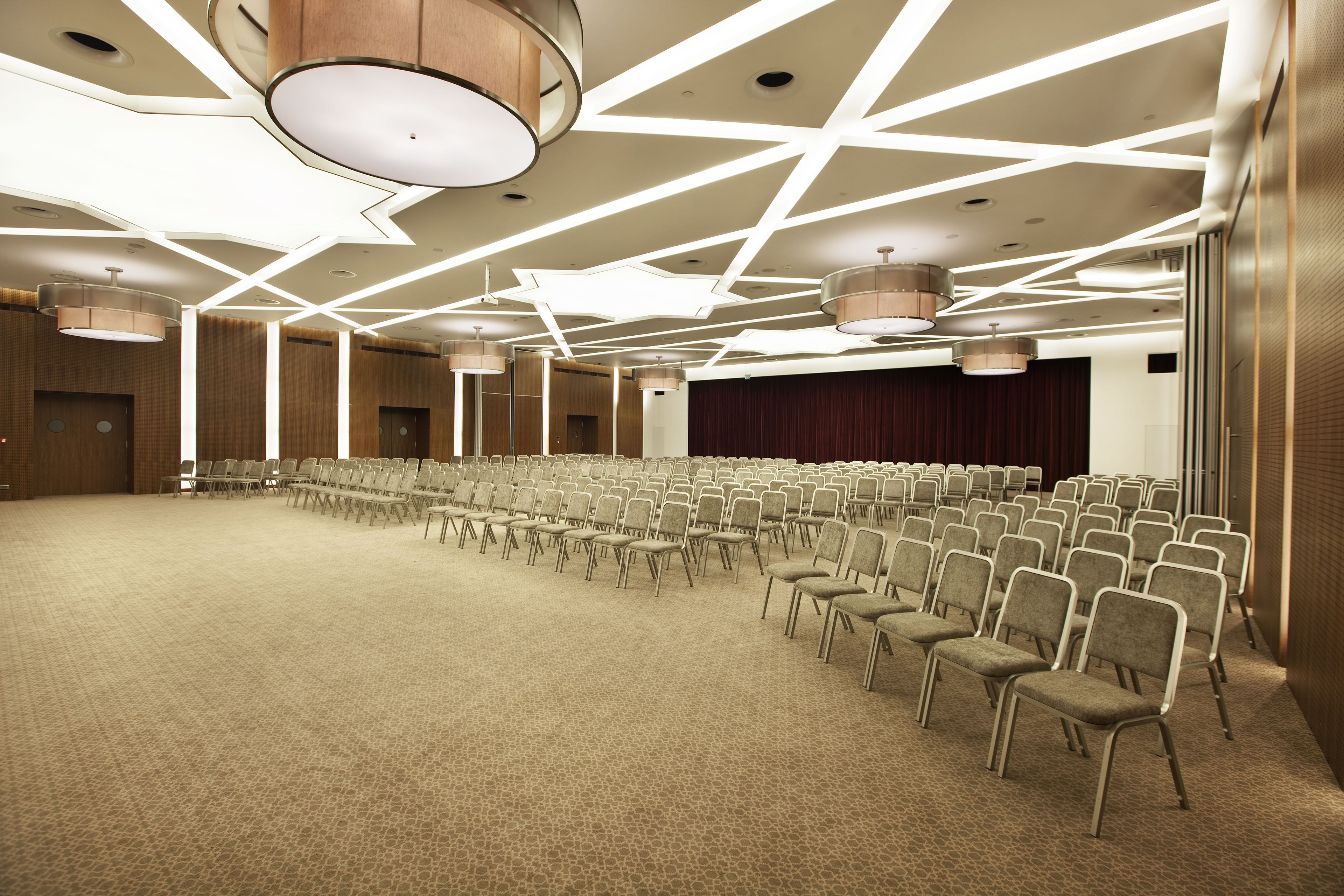 A large conference room with rows of chairs, a stage, and a modern ceiling design.