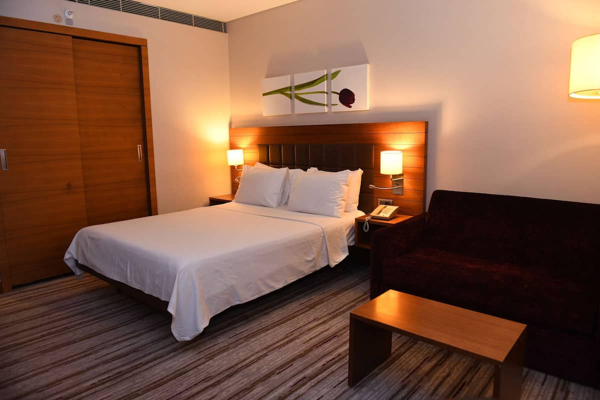 A hotel room with a bed, bedside lamps, a wooden wardrobe, a red sofa, and a small table.