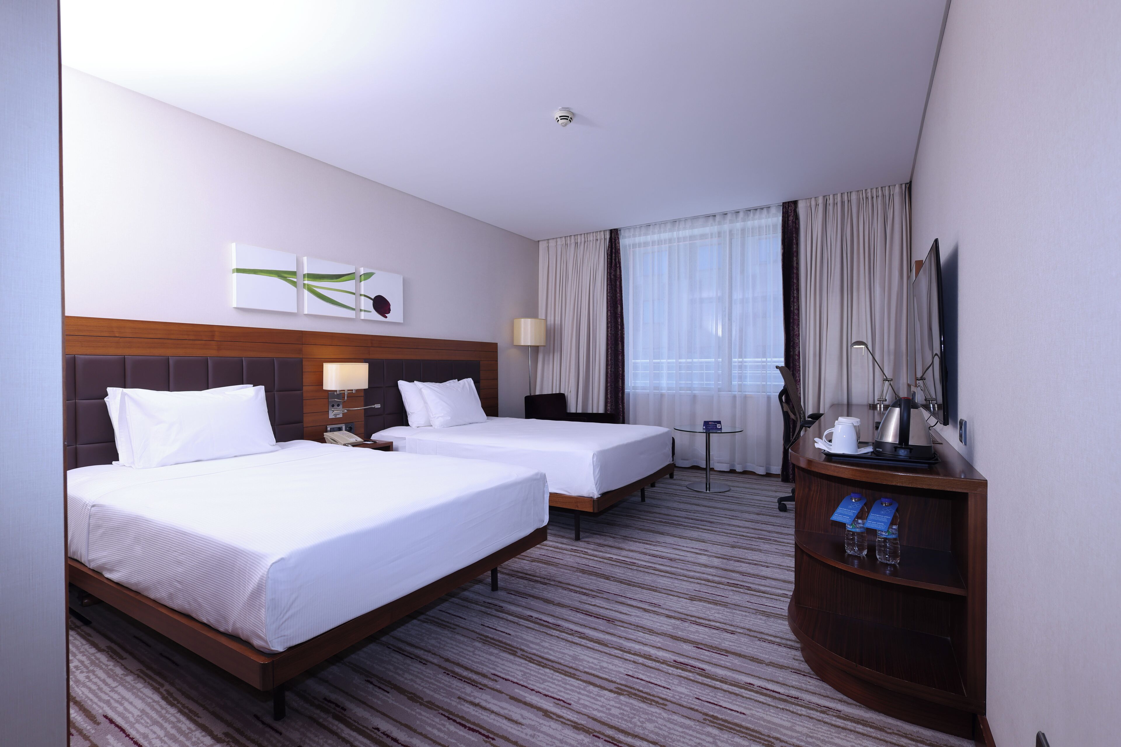 A hotel room with two beds, a desk with a lamp, a coffee maker, and a small table with a mirror and a telephone.