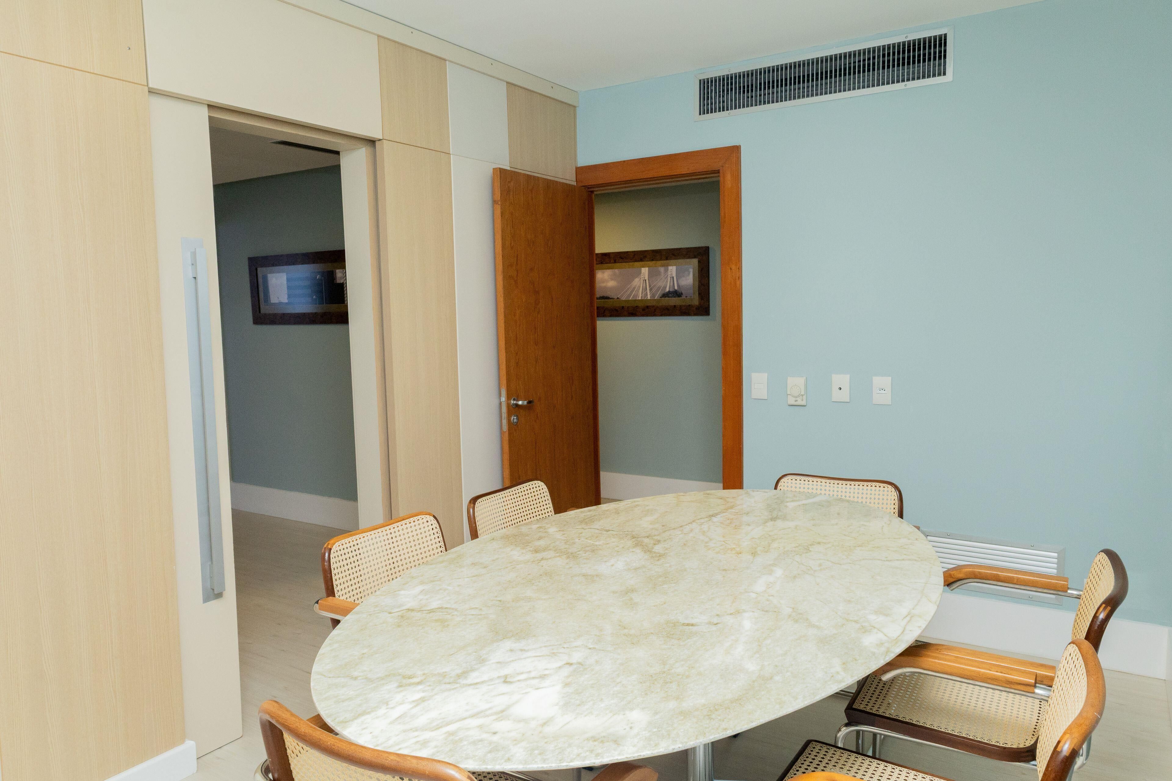 Un salón de conferencias con una mesa de mármol, sillas de mimbre y una puerta que da a otra habitación.