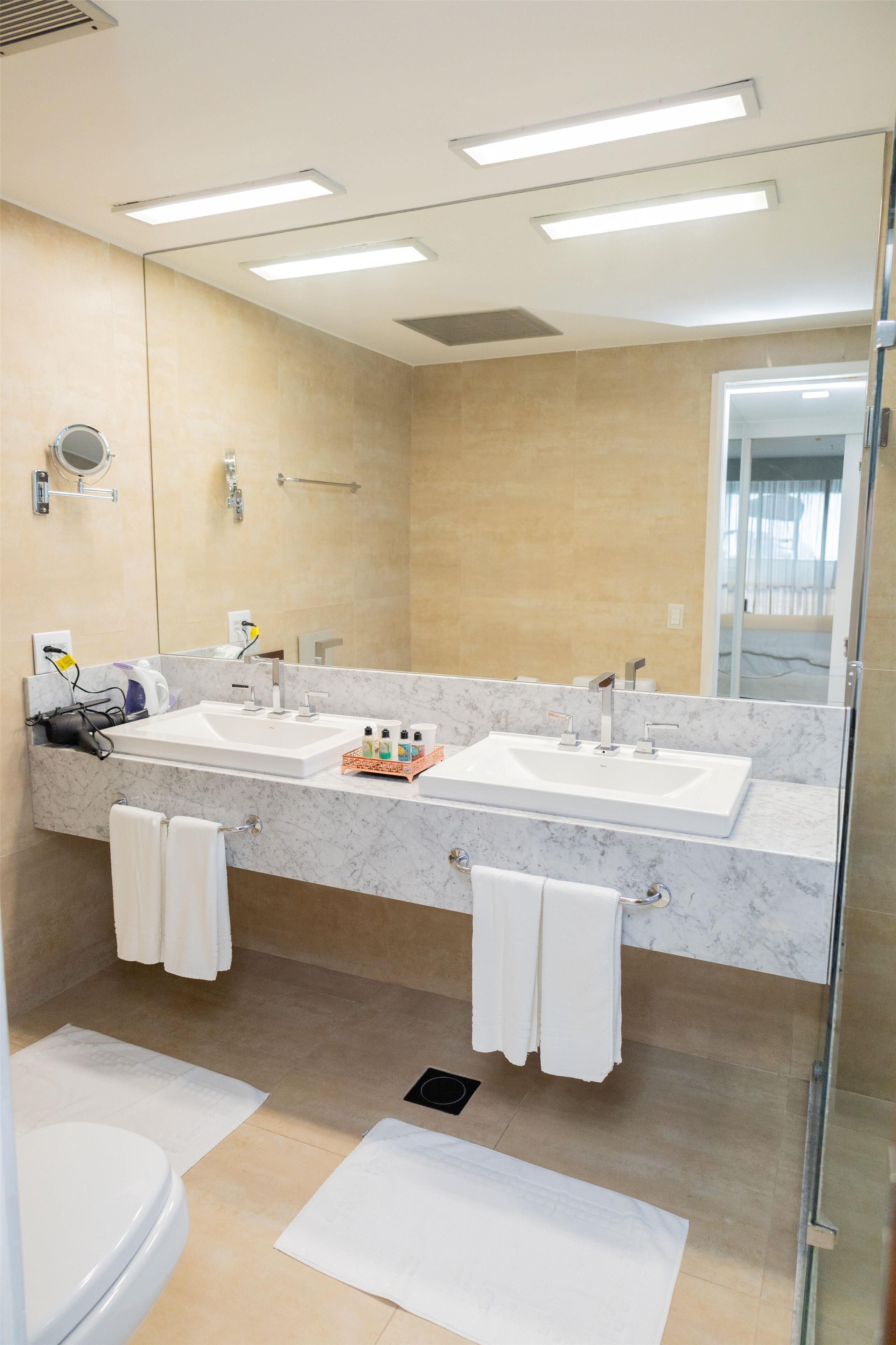 Uma casa de banho moderna com duas pias, um espelho grande e cabine de duche em vidro.