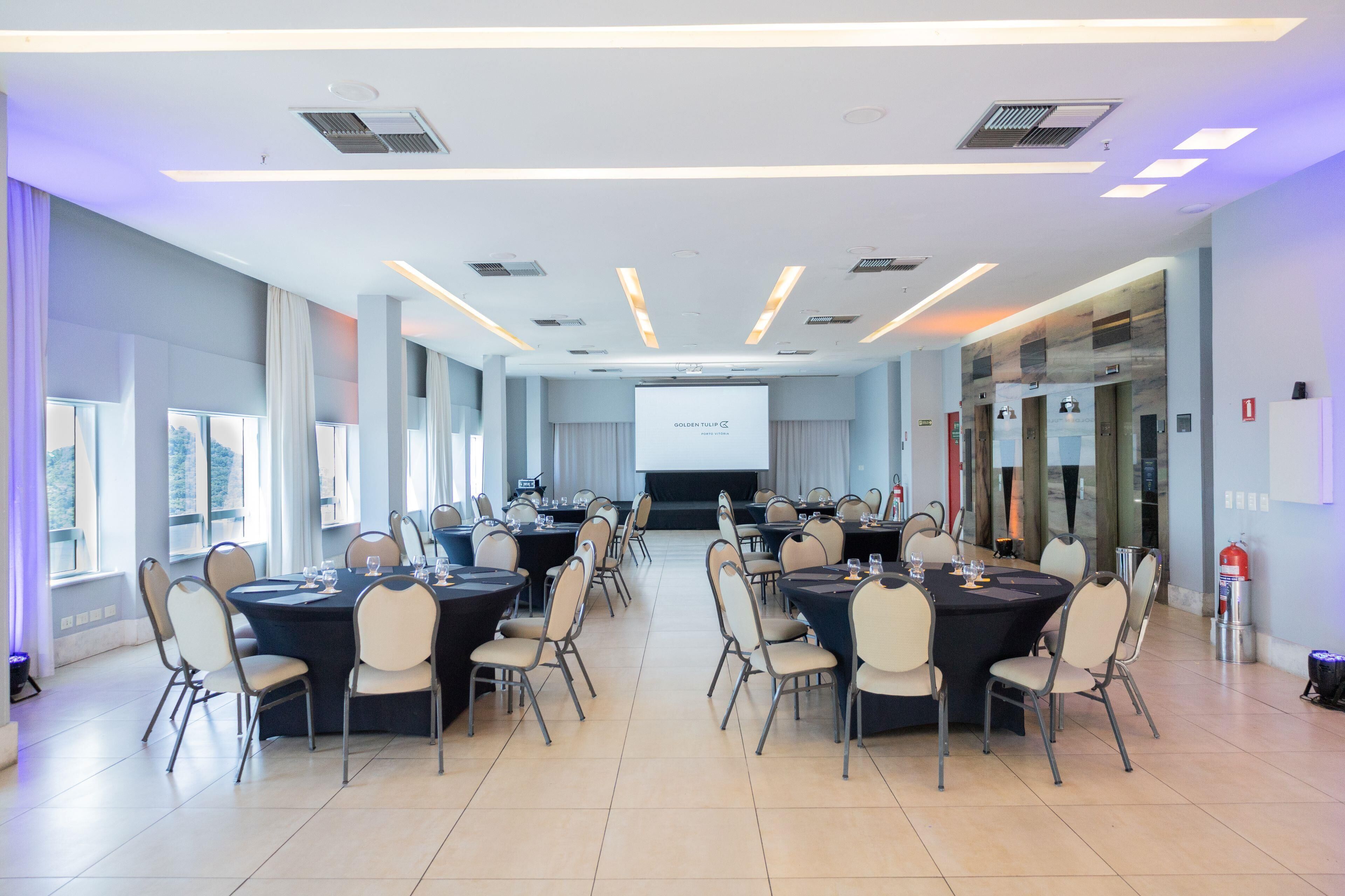 Un salón de conferencias con varias mesas y sillas, una pantalla de proyector y un extintor.