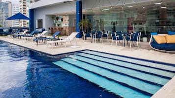 Una piscina interior amb gandules i un sofà, envoltada d'un edifici modern amb grans finestres.