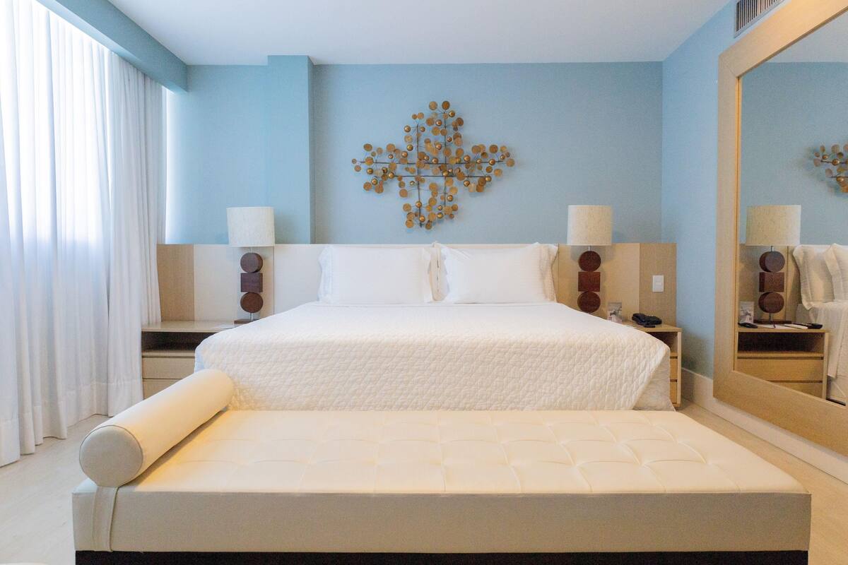 A bedroom with a large bed, two bedside tables, a wall-mounted lamp, and a mirror.