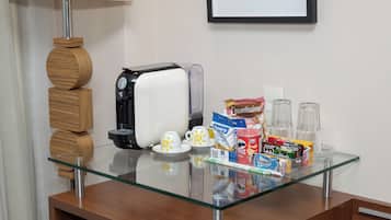 Una mesa con cubierta de vidrio, una tostadora, tazas blancas, una cafetera y diversos alimentos.